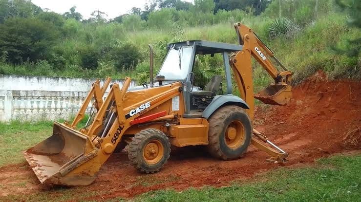 Retroescavadeira Case parada em área gramada, ao lado de um trecho de terra vermelha recém-movida.